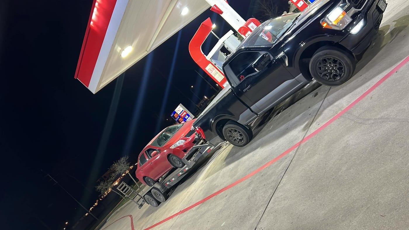 Black tow truck loading a car for pickup at a Houston gas station at night